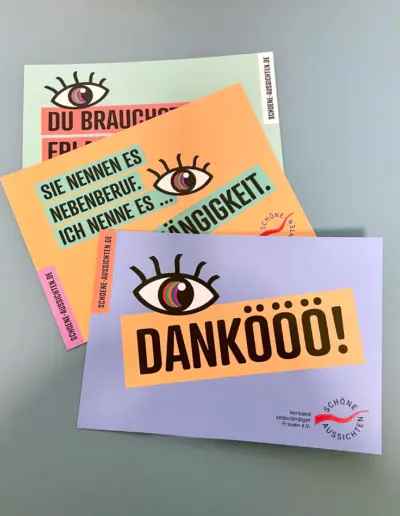 Bunte Postkarten mit Augen-Motiv und motivierenden Texten wie ‚Du brauchst frische Augen‘ und ‚Dankoooo!‘ für Frauen e.V. auf grauem Hintergrund
